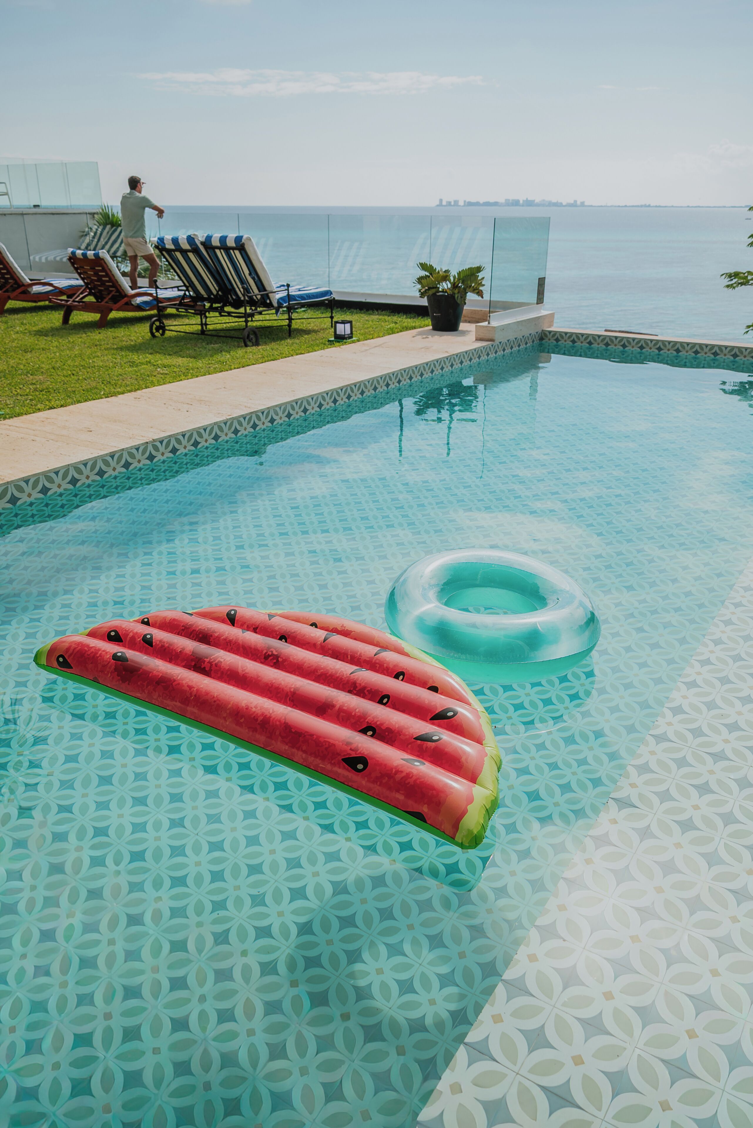 A swimming pool with a glass barrier, lounge chairs, and a view of the sea.