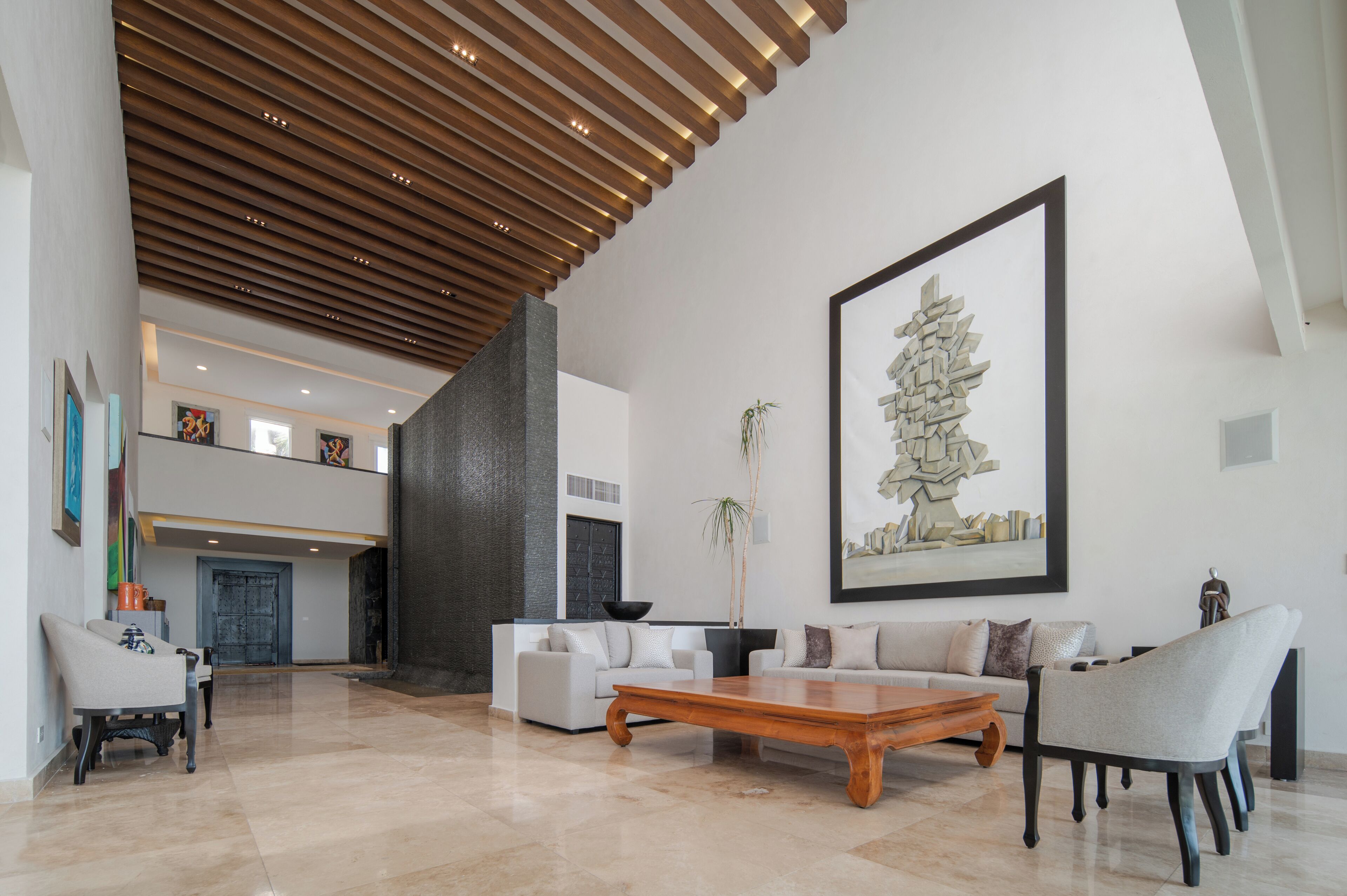 Uma sala de estar ampla, com pé direito alto, móveis modernos e um grande quadro abstrato.