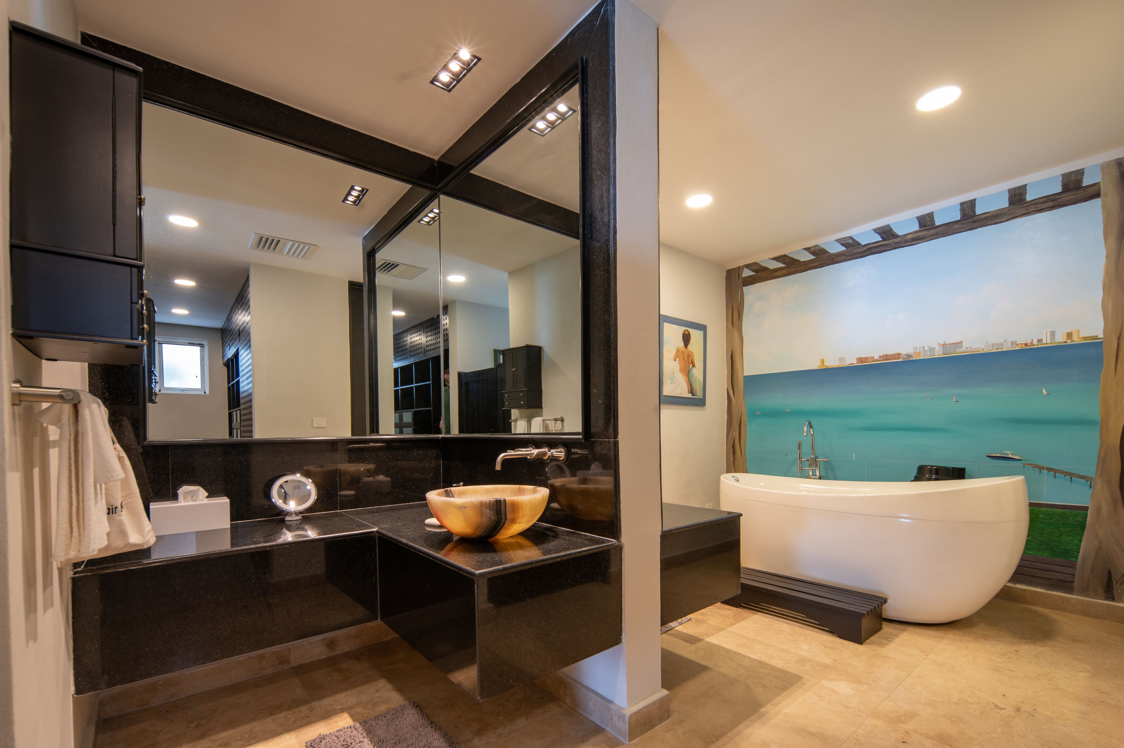 Un baño moderno con un espejo grande, un lavabo de madera, una bañera blanca y un mural de paisaje urbano en la pared.
