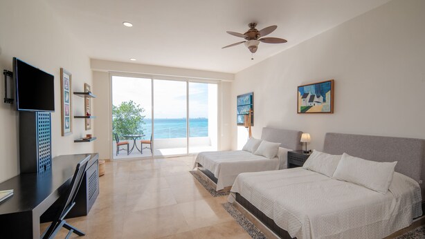 A hotel room with two beds, a desk, a TV, and a balcony with a view of the ocean. - Villa Chan Kah (Isla Mujeres)