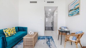 A modern living room with a teal sofa, a wooden crate, and a wicker chair. - Cozy studio at Damac Hills (Dubai)