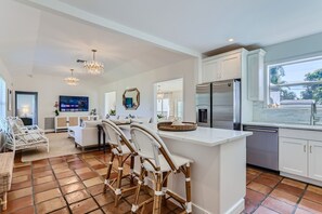 Uma cozinha moderna com armários brancos, uma ilha central com banquetas e uma geladeira embutida, além de uma grande janela que oferece vista para o exterior.