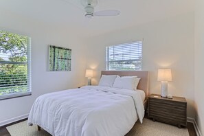 A bedroom with a bed, two bedside lamps, a ceiling fan, and a window with blinds.