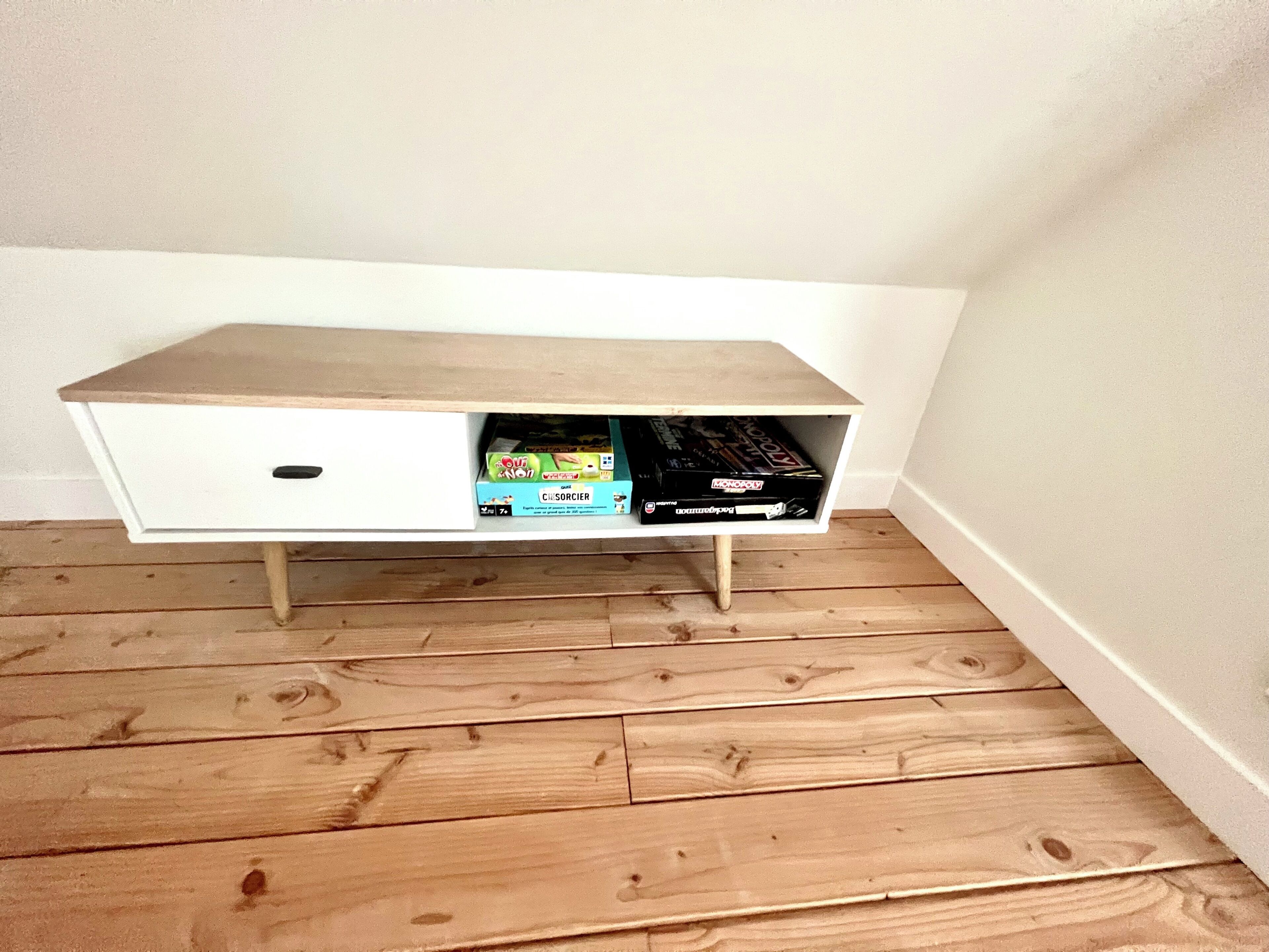 Un módulo de almacenamiento blanco con repisa superior de madera y dos compartimentos, uno con un cajón blanco y el otro con cajas de juegos.