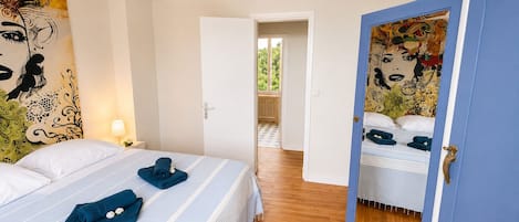 A hotel room with a bed, a door leading to a balcony, and a large mirror with artwork.
