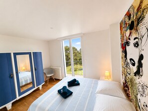 A hotel room with a bed, a wardrobe, a chair, a radiator, and a view of the outdoors. - La Villa Océane, Elegante, Plages, Gr34, 2-8 Pers (Clohars-Carnoët)