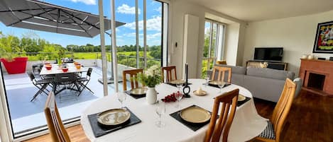 A dining area with a table set for six, large windows, and a view of the outdoors.