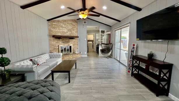 A spacious living area with a high ceiling, a fireplace, a sofa, a coffee table, and a TV mounted on the wall. - Furnished 4BR Pool Home Near Randolph AFB for PCS, TDY & Military Families in SA (Universal City)