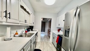 A modern kitchen with stainless steel appliances, white cabinetry, and a central island. - Furnished 4BR Pool Home Near Randolph AFB for PCS, TDY & Military Families in SA (Universal City)