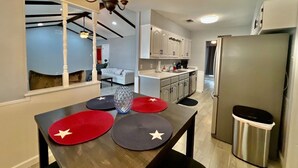 A modern kitchen with a dining table, cabinets, and a stainless steel refrigerator. - Furnished 4BR Pool Home Near Randolph AFB for PCS, TDY & Military Families in SA (Universal City)