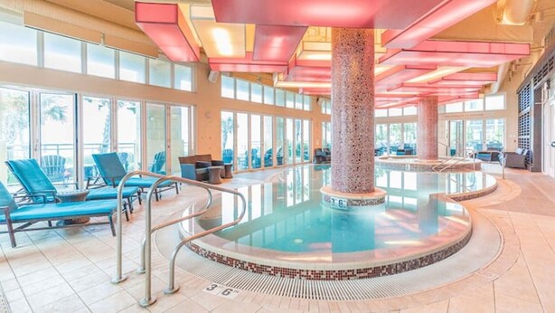 A large indoor pool with a central column, sun loungers, and a tiled floor. - Oceanfront Luxury at Hilton Oceanaire Resort – Two Stunning Oceanview Balconies! (Virginia Beach)