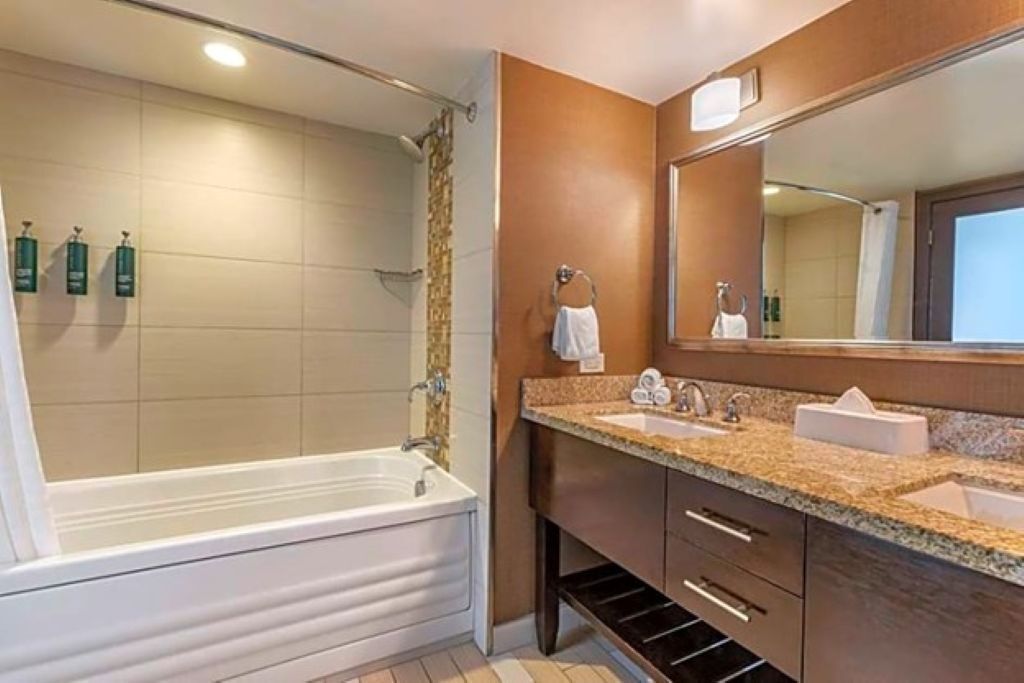 A modern bathroom with a bathtub, two sinks, a vanity with drawers, a large mirror, and a shower curtain.