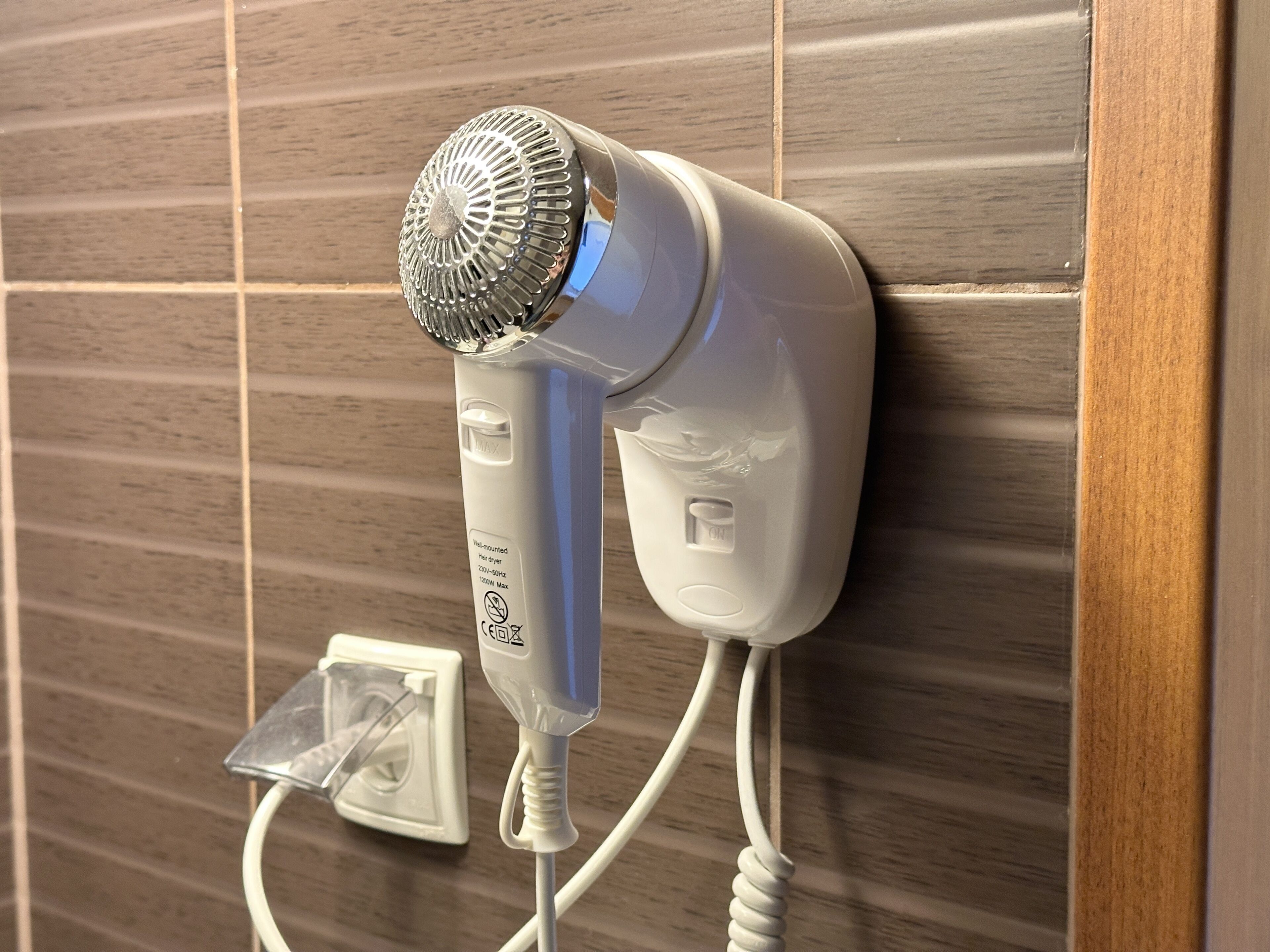 A hair dryer mounted on a tiled wall, connected to a power outlet.