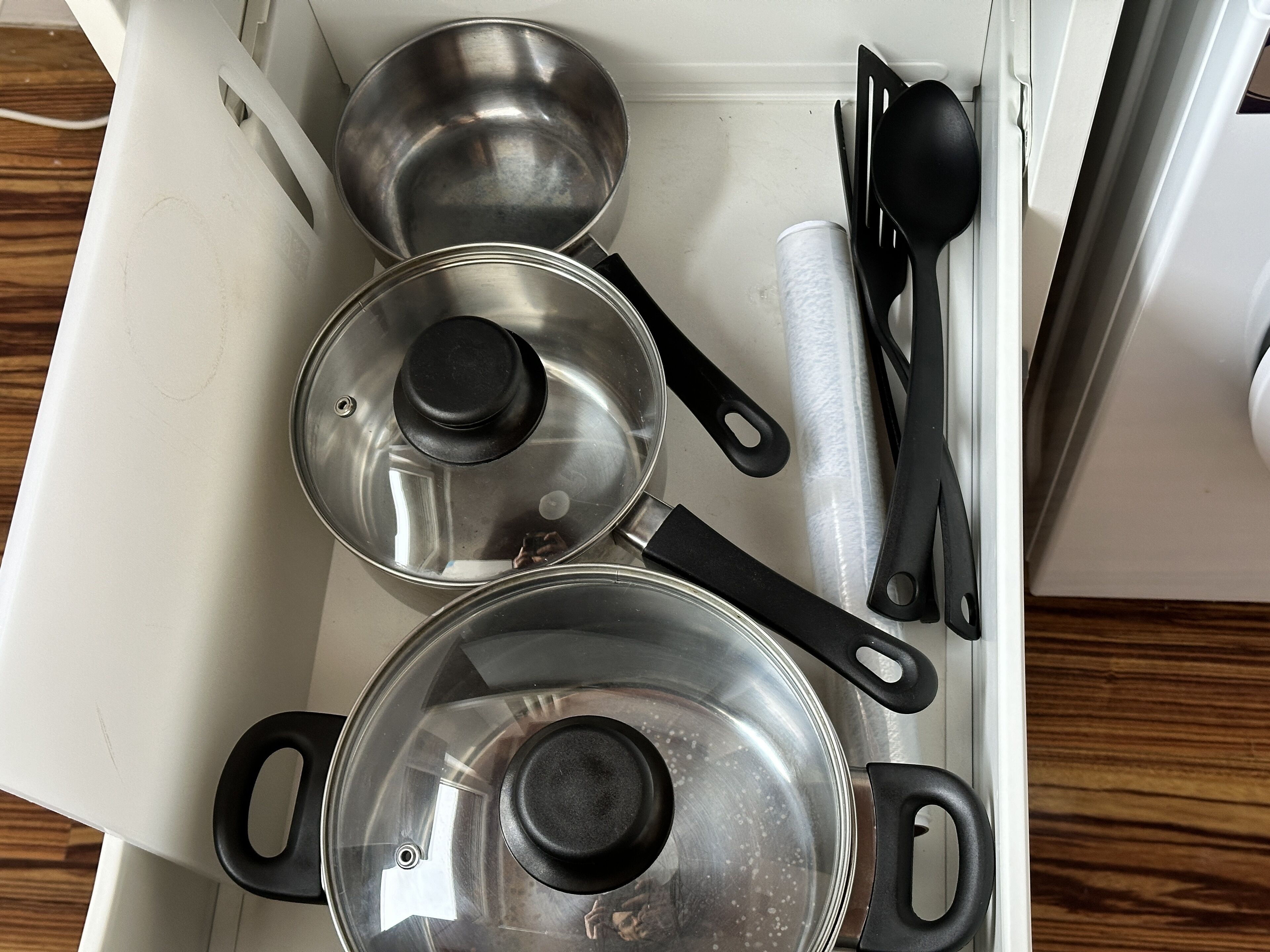 A kitchen drawer containing pots, pans, and cooking utensils.