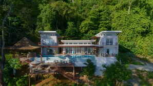 A modern two-story house with a pool, surrounded by lush greenery.