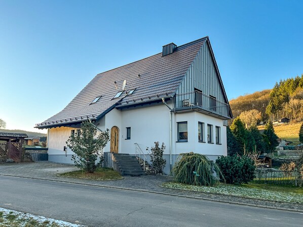 A two-story house with a sloped roof, a satellite dish, and a small balcony. - House Meerten (Neroth)