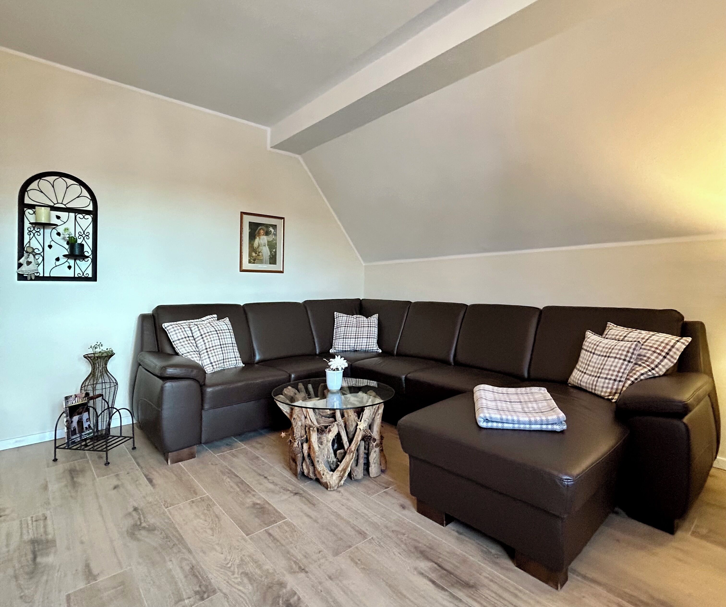 Ein modernes Wohnzimmer mit einem Ecksofa, einem Glastisch und einem dekorativen Metallregal.
