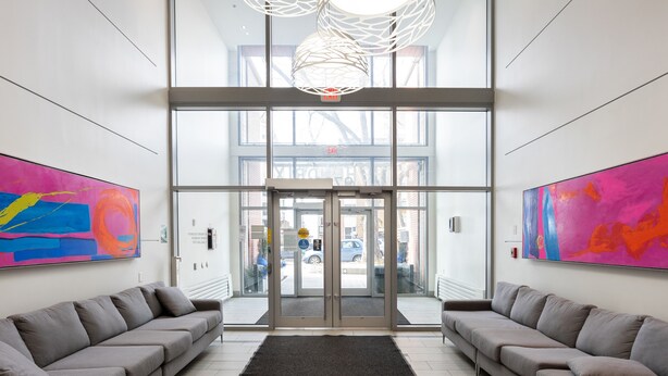 A modern lobby with two sofas facing a glass door entrance, a black rug, and abstract paintings on the walls. - Corporate Stays Hendrix Aparments (Edmonton)