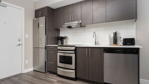 A modern kitchen with dark wood cabinets, stainless steel appliances, and a white tiled backsplash. - Corporate Stays Hendrix Aparments (Edmonton)