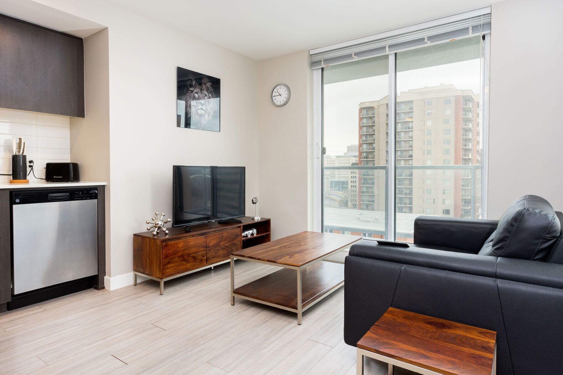 A modern living room with a sofa, a coffee table, a TV, and a kitchen area with a dishwasher and toaster.
