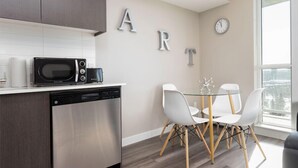 A modern kitchen with a microwave, dishwasher, and a dining area with a glass table and white chairs. - Corporate Stays Hendrix Aparments (Edmonton)