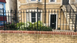 A corner building with a brick facade, black metal fence, and a small garden area with plants. - 2 Guests - 5min To The Beach - Fireplace (Scarborough)