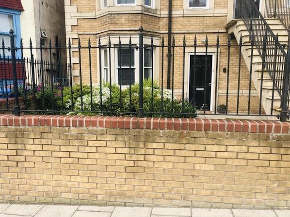 A corner building with a brick facade, black metal fence, and a small garden area with plants.