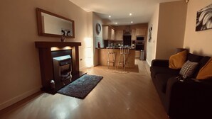 A living room with a fireplace, a kitchen in the background, and a sofa with cushions. - 2 Guests - 5min To The Beach - Fireplace (Scarborough)
