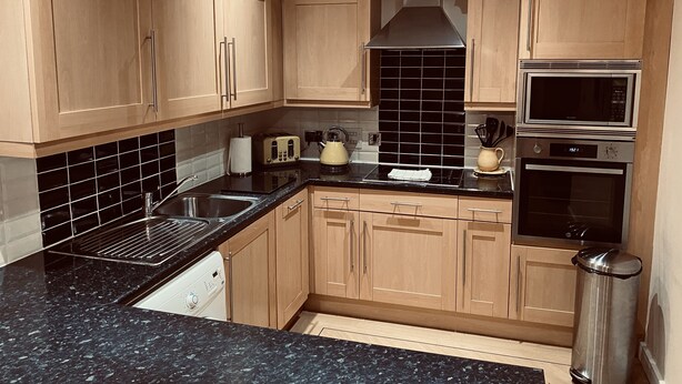 A modern kitchen with wooden cabinets, a black tiled backsplash, stainless steel appliances, and a granite countertop. - 2 Guests - 5min To The Beach - Fireplace (Scarborough)