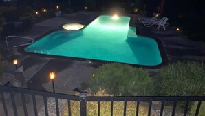 Une piscine dont le bord est illuminé, entourée d’une terrasse aménagée avec des chaises et un petit foyer extérieur.