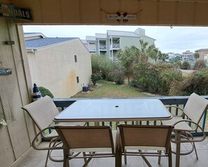 Un patio exterior con mesa y sillas, con vista a una zona residencial con casas y un letrero que dice 'Welcome to the Beach'.