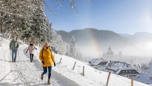 A snow-covered path with a rustic fence, a building with a dome, and a clear sky. - Holiday apartment Ammerglück "Classic" in Oberammergau (Oberammergau)