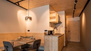 Una cocina compacta con una isla de madera, un comedor con mesa y sillas, y una puerta visible que da a otra habitación.