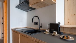 Una cocina compacta con un lavamanos negro, armarios de madera y una cafetera.