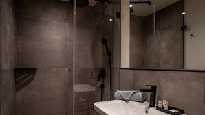 Un baño moderno con ducha envuelta en vidrio, un lavabo blanco y un espejo grande.