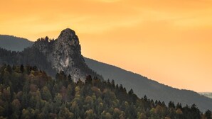 A mountain landscape with a prominent rocky peak and dense forest at the base.