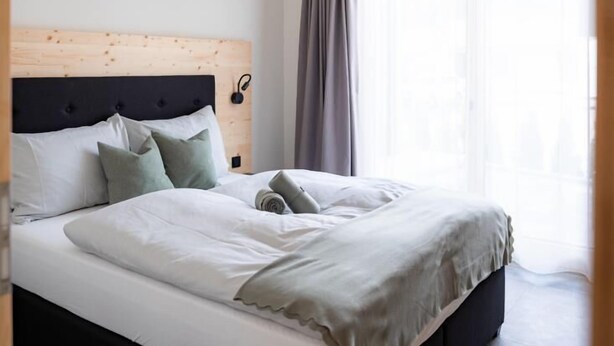 A modern hotel room with a large bed, a wooden headboard, and a large window with curtains.