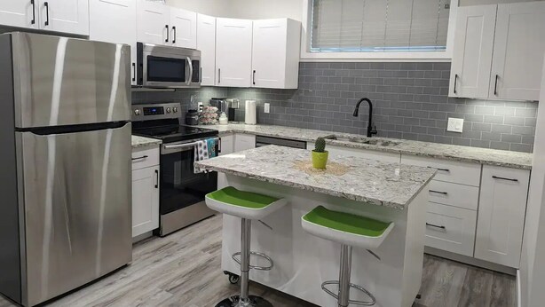 A modern kitchen with white cabinets, stainless steel appliances, a granite countertop, and a window with blinds. - Confortable brand-new 1-bedroom close to downtown
(Saskatoon)