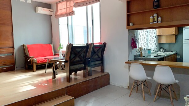 Un espacio habitable compacto con sofá, mesa de comedor, sillas, zona de cocina y una escalera.