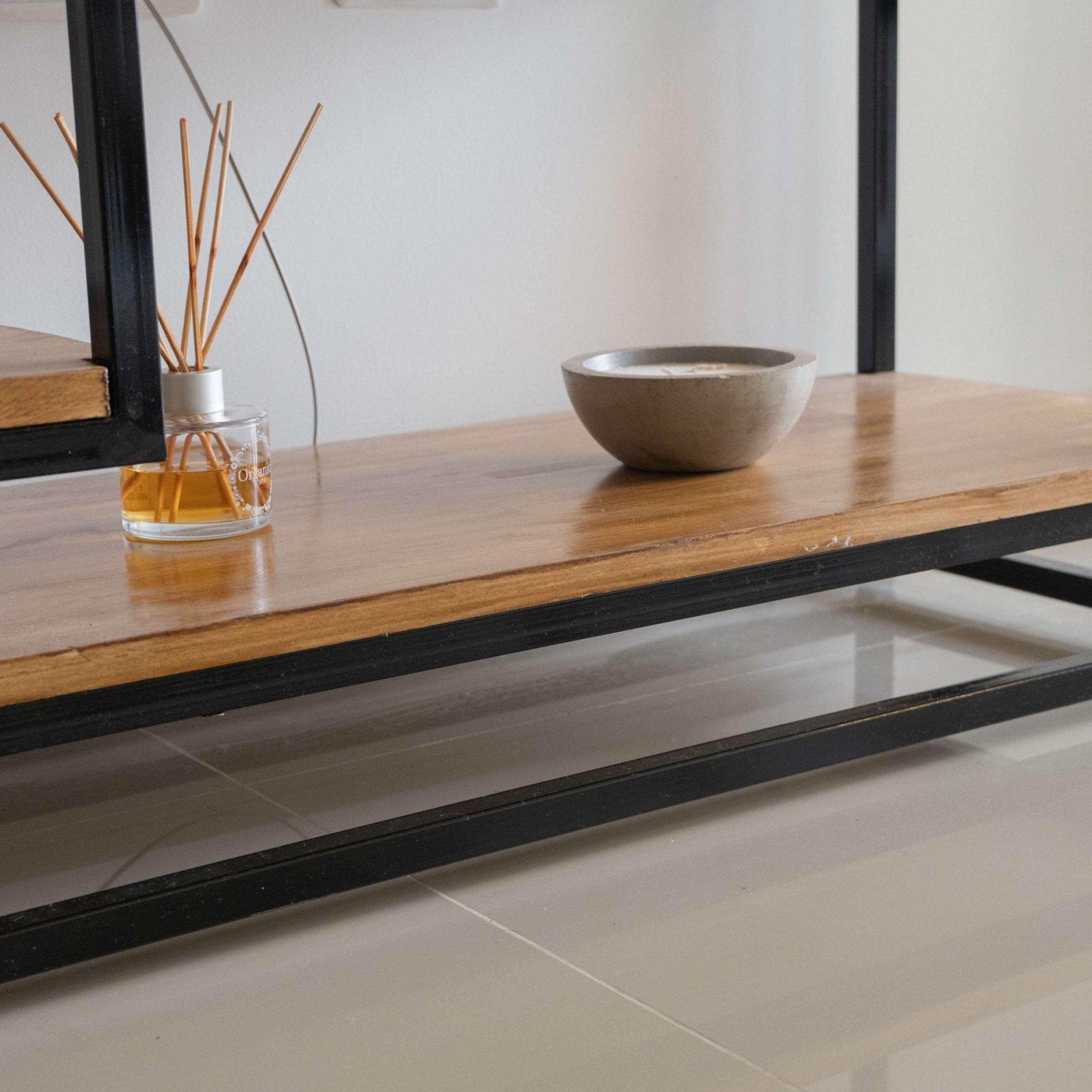 A wooden table with a glass bottle and reed diffuser, and a ceramic bowl on it.