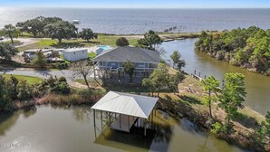 Une maison avec une piscine et une jetée qui s’avance dans l’eau, entourée d’arbres et offrant une vue dégagée sur l’océan.