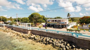 A coastal hotel with a white facade, a covered outdoor seating area, and a view of the sea. - Studio #3 Anacaona w/ Garden- Guayacan Guesthouse (Vieques)