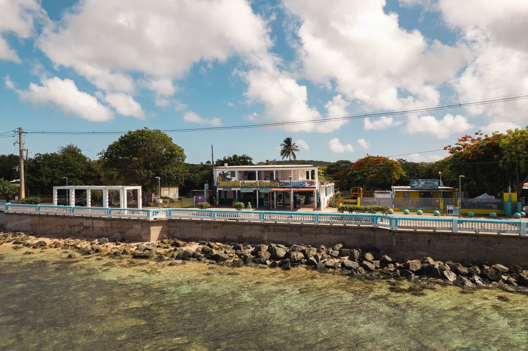 Ein Küstengebäude mit freiem Blick auf das Meer, eine Brücke mit Geländer und ein Schild für einen Wassersportsverleih.