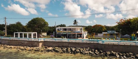 A coastal building with a clear view of the sea, a bridge with a railing, and a sign for a water sports rental service.