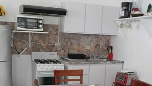 Une cuisine compacte équipée d’une cuisinière, d’un four à micro-ondes et d’un évier. On y trouve une table à manger avec des chaises, ainsi qu’un chemin de table décoratif.