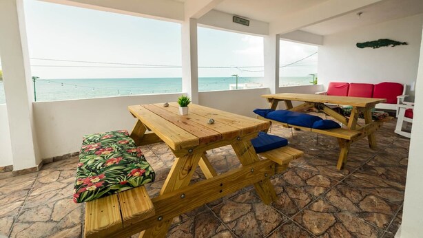 Une terrasse avec des tables et des bancs en bois, un canapé rouge et une vue sur la mer.
