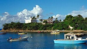 A coastal scene with boats on calm water, a white building with a lighthouse, and lush greenery. - Oceanview Apartment & Garden (Vieques)