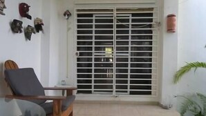 A room with a large window with metal bars, a wooden chair, a glass table, and a potted plant. - Oceanview Apartment & Garden (Vieques)