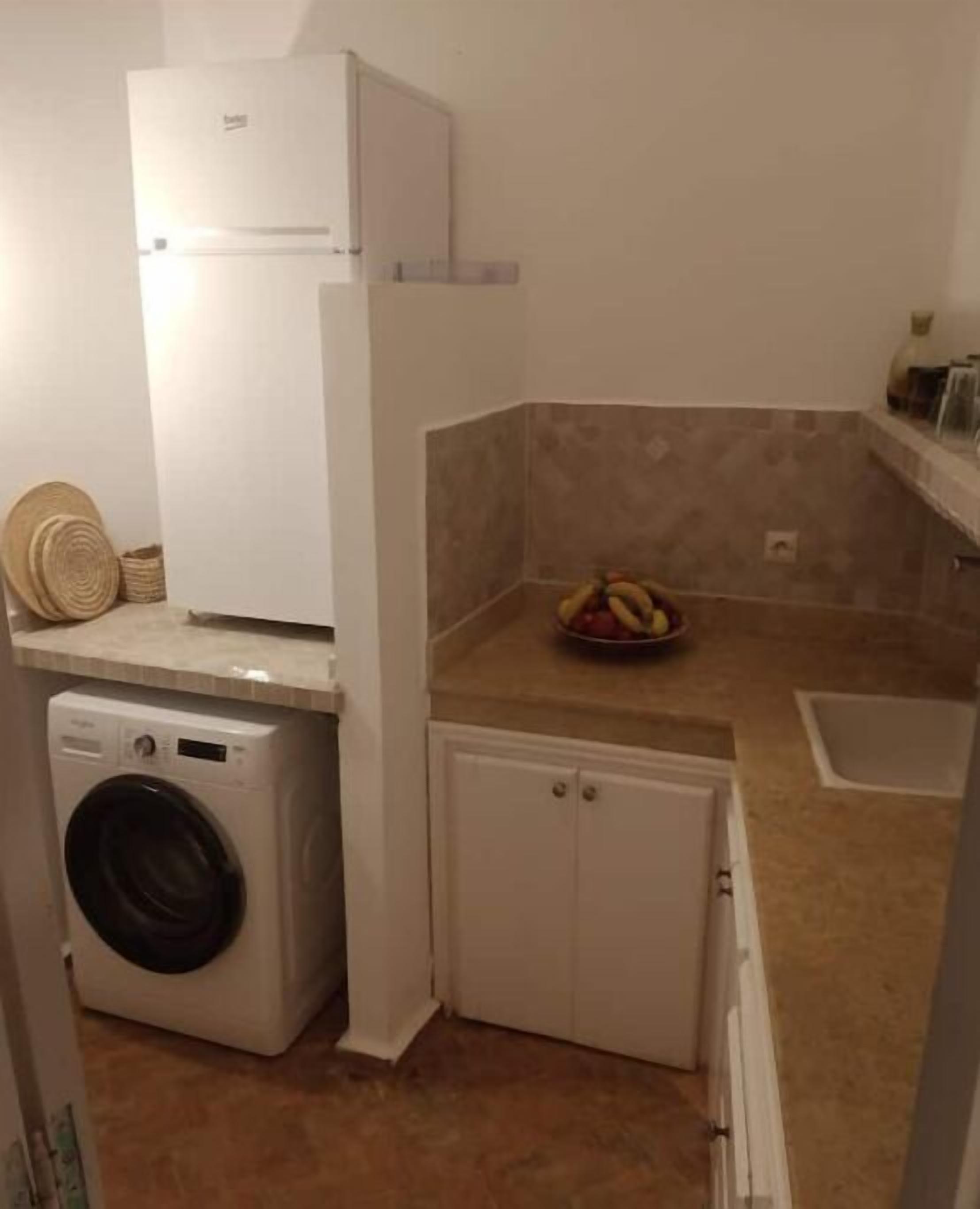A compact kitchen with a washing machine, a small cabinet, and a fruit bowl on the counter.