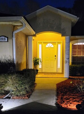 A house with a yellow front door, a small porch, and a number '1915' on the wall.